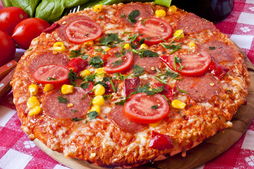 木制砧板上的西红柿和意大利腊肠披萨图片