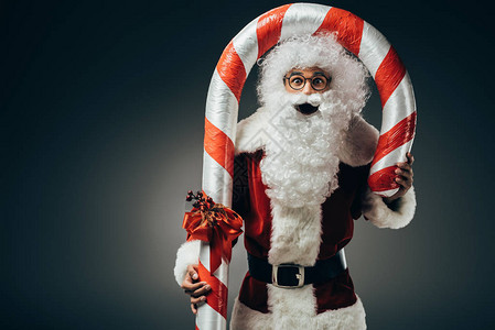 穿着盛装的圣坦达克劳斯SantaClauus站在大条纹的圣诞棍上与图片