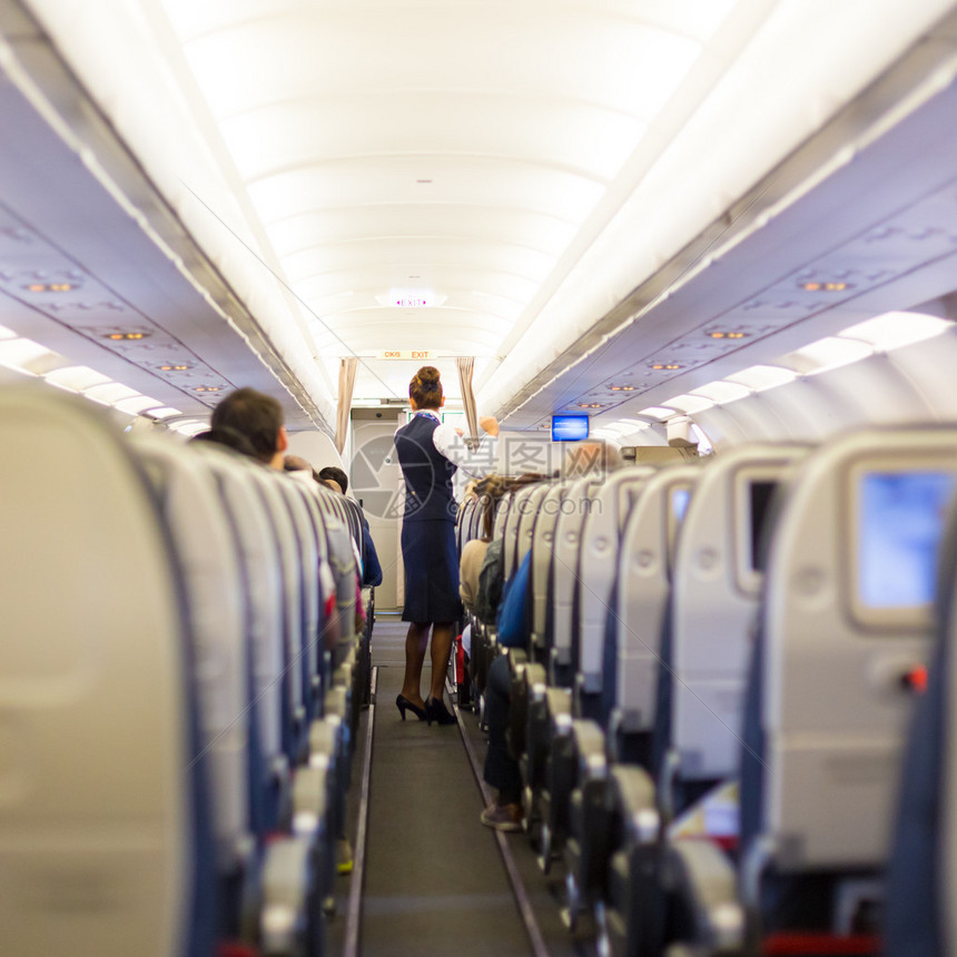 乘客坐在座位上的飞机和身着制服的空姐在过道图片