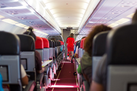 飞机内有乘客坐在座位上和穿红色制服的空姐图片
