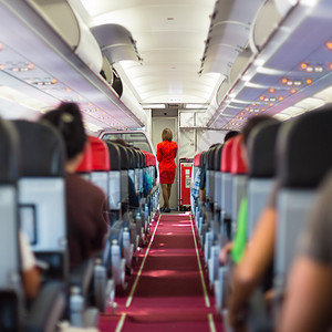 客座乘客和在过道穿红色制服的空姐的飞图片