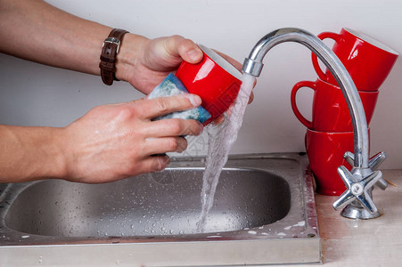 男人的手在洗红杯子在厨房水槽里用自图片