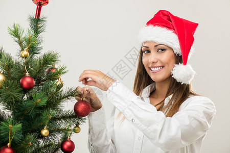 一位身戴圣塔帽装饰圣诞树的年轻背景图片