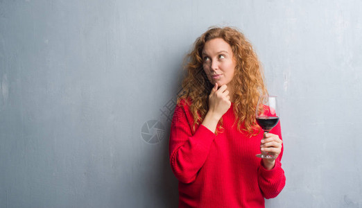红发女青年在灰墙上喝着一杯酒严肃的面孔想问题非图片