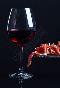 黑色背景中的熏火腿和一杯红酒图片