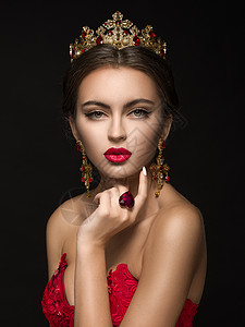 穿着金冠的漂亮女孩和深色背景的耳环在心脏形状上摇铃红裙子背景图片