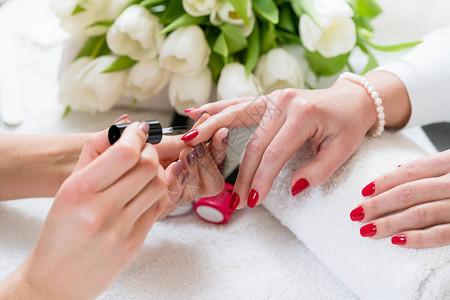 一位熟练的美术师用优雅的红色指甲油贴近一名年轻女子在时尚美容院图片