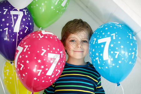 快乐的孩子男孩与束在五颜六色的气球上7岁生日的画像微笑的学童玩得开心图片