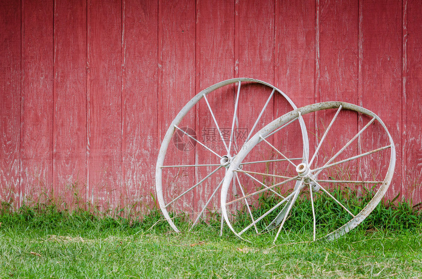 有老白色马车轮和绿草的红色谷仓墙壁图片