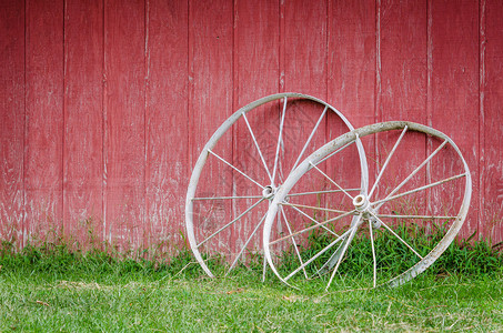 有老白色马车轮和绿草的红色谷仓墙壁图片