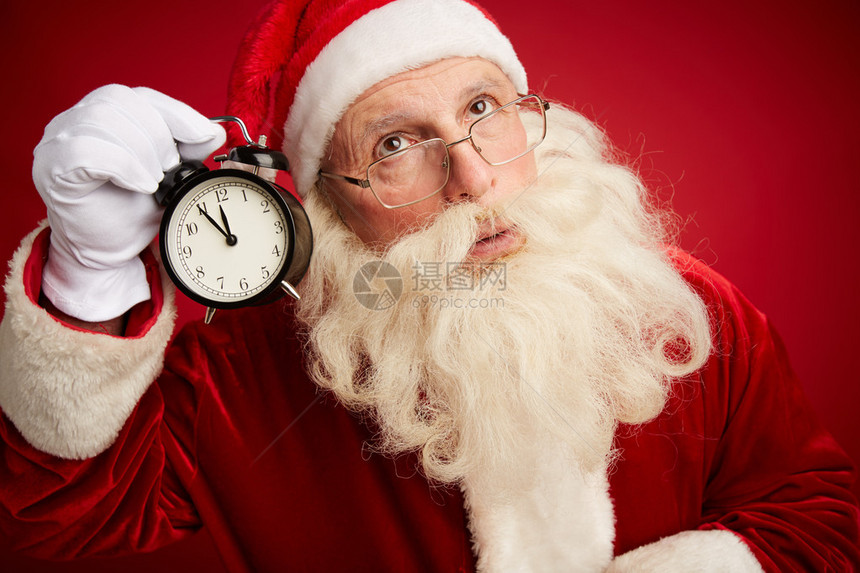 带着闹钟的圣诞老人用红色背景的耳朵按着他的耳朵向Xm图片