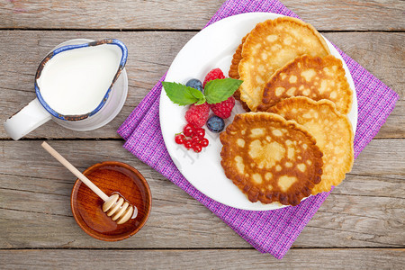 覆盆子蓝莓牛奶和蜂蜜糖浆煎饼在木桌上图片