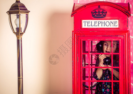 一个小女孩在传统的红色电话亭高清图片