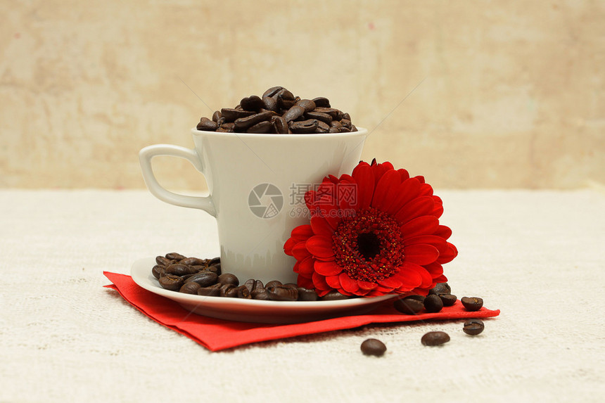 白色杯子咖啡豆和亚麻桌布上的红花图片