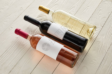 白色木质表面上装有红白和玫瑰酒的瓶子图片