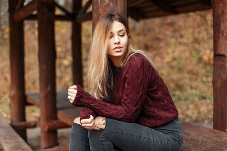 穿着时装毛衣和牛仔裤的时髦年轻女子坐图片