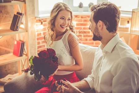 英俊优雅的向漂亮女友求婚给她玫瑰和微笑当他们在家里有浪漫约会时图片