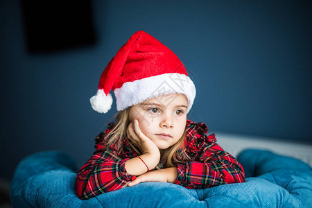 穿着圣塔帽的漂亮女孩的肖像等着圣诞老人看着家图片