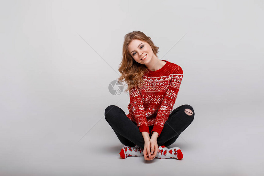 穿着红色毛衣的年轻美女在工作室的地板上坐着一张印有图片