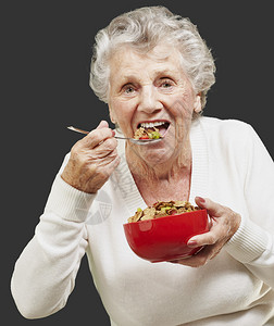 在黑色背景下用红碗吃麦片的老妇人图片