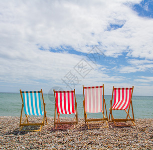四张老式甲板椅面对海洋在一块石子沙滩上图片