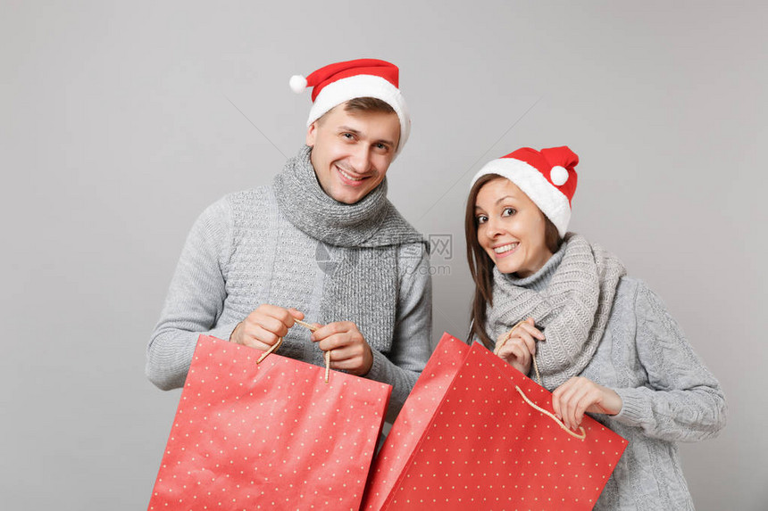 快乐有趣的情侣女孩穿着红色圣诞帽灰色毛衣围巾隔离在灰色的墙壁背景上图片