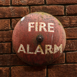 质朴的老式火警钟靠在红砖墙上图片