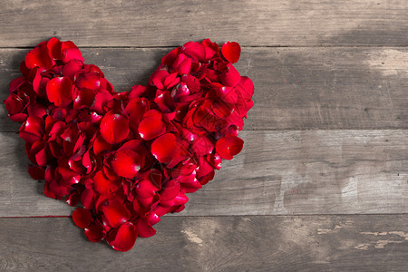 旧木背景上由红玫瑰花瓣制成的情人节心图片