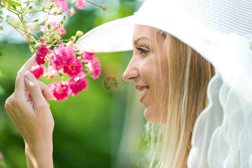 美丽的自然年轻女子的肖像在玫瑰花园里戴着白帽图片
