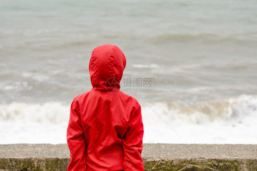 穿着红色夹克的男孩带着头罩站在码头后面图片