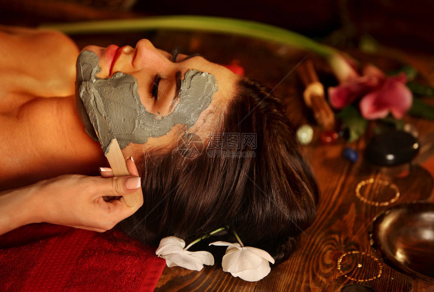 水疗沙龙中女人的泥面膜用粘土全脸按摩背部豪华芳香疗法内部的女孩与东方疗法室女与躺在木制水疗床图片