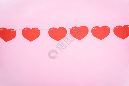 美丽的装饰红心挂在粉红色背景的绳索上图片