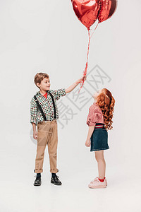 美丽的小女孩看着男孩拿着心形的气球图片