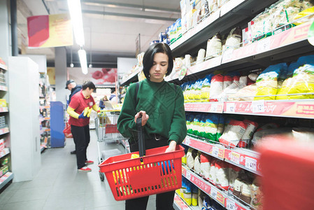女孩在超市买碎粒从商店货架上选择食物一个提着篮子的女图片