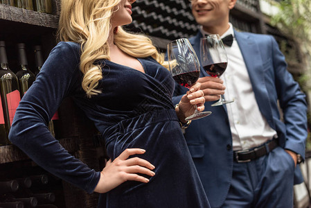 美貌成人夫妇在葡萄酒储藏架前饮酒的图片