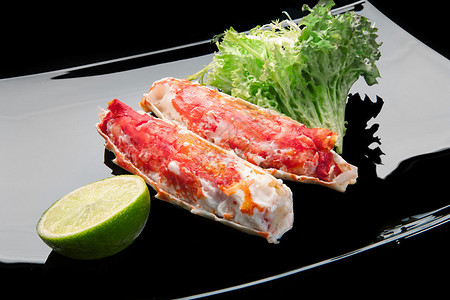 红帝王蟹肉放在黑盘上配上酸橙和沙拉叶背景图片
