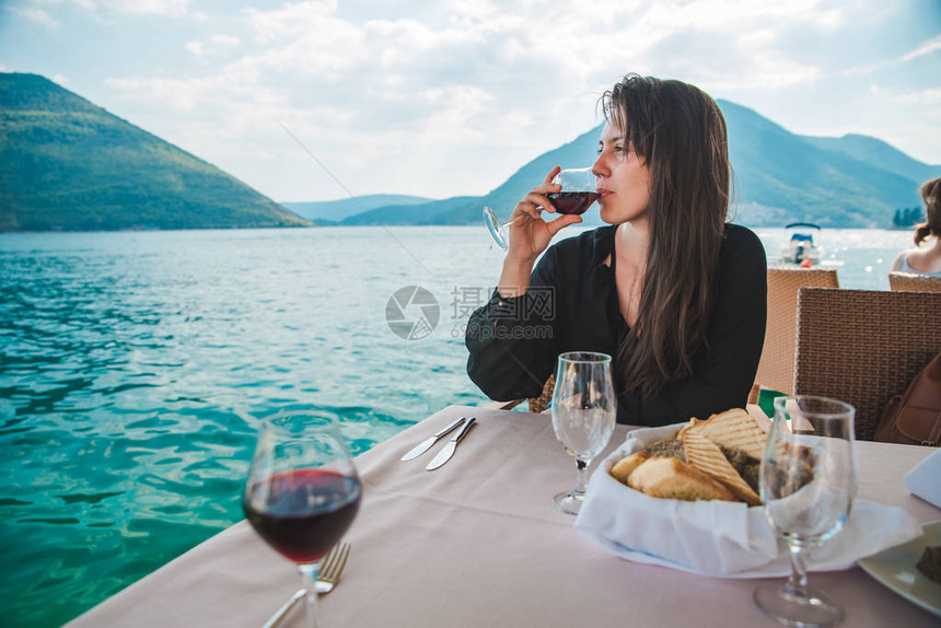 在海边餐厅喝红葡萄酒的年轻美女山上有背景的山峰图片