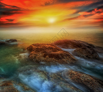 沙滩上闪耀着日出照亮的一连串巨石在海图片