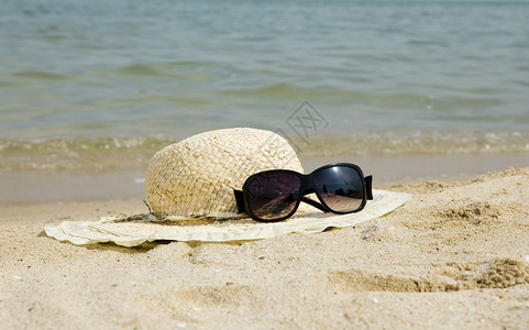 太阳镜和草帽躺在海边的沙滩上图片