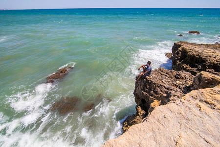 勇敢的男人喜欢看着悬崖尽头的海洋在美丽的岩石海滩图片