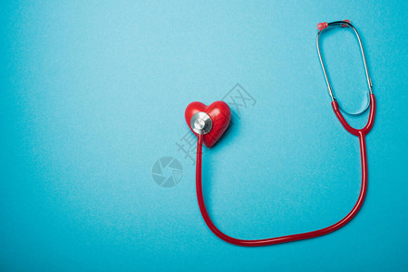 与蓝色背景的红听诊器相连的装饰心脏顶部视图背景图片