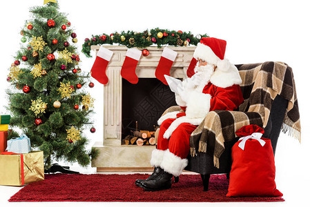 圣诞老人坐在壁炉旁的扶手椅上使用平板电脑图片