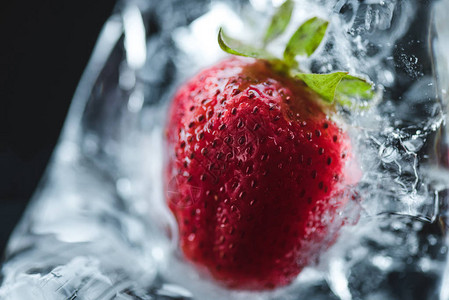 黑色冰块中冷冻红草莓的特写镜头图片