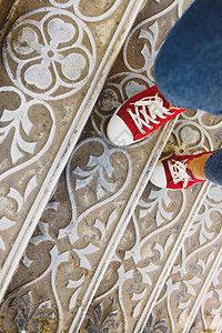 在古董金属楼梯上穿牛仔裤和红运动鞋的长腿图片
