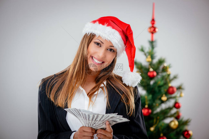 穿着圣塔帽和拿着钱的成功的商业女商图片