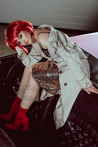穿着红色假发的漂亮时装美女坐在老式汽车上看着图片