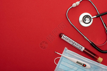 听诊器带温度计的医用面罩和红色背景血试管上的冠状字图片