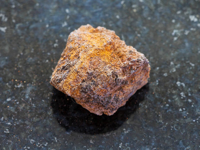 天然矿物岩石标本的宏观拍摄深色花岗岩背景上的粗糙褐铁矿图片