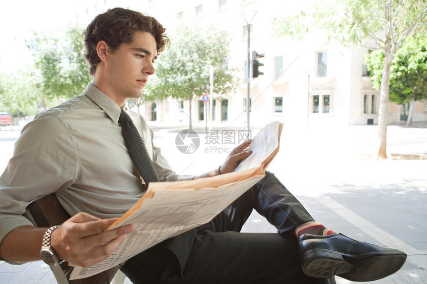 一位年轻商人在城里坐在长椅上看金融报纸时的侧面景象图片