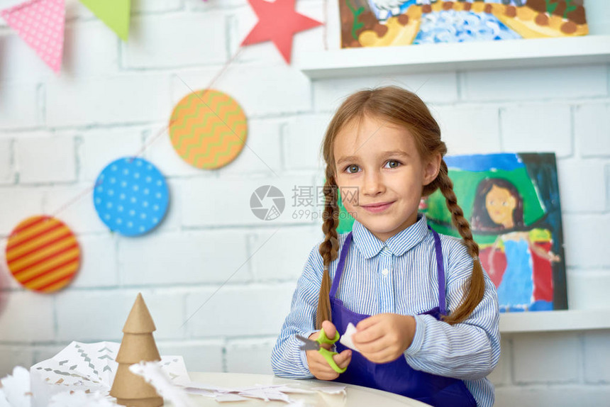 漂亮小女孩在学前艺术和工艺课上制作手工圣诞装饰品时对着镜头开心地微笑的肖图片